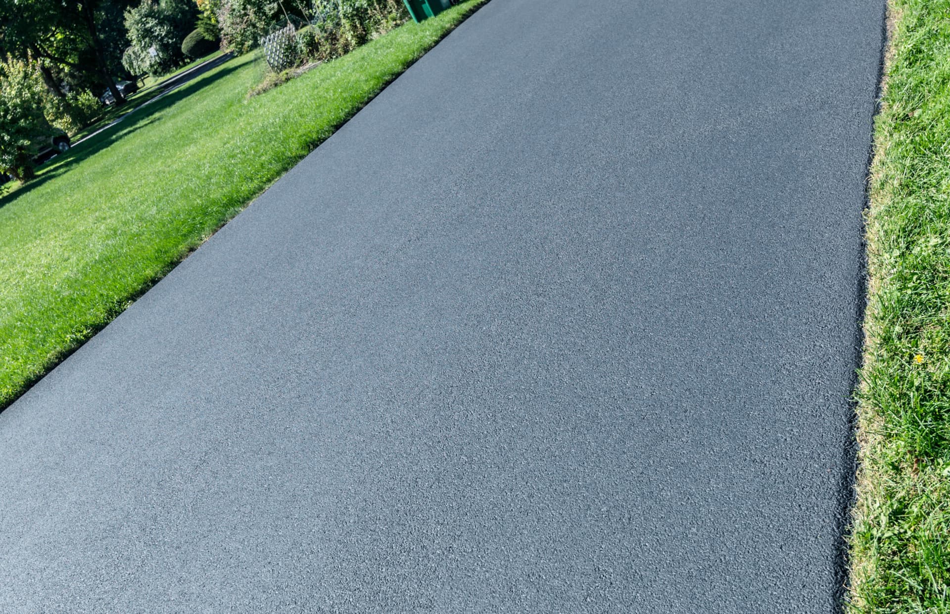A close view along a smooth grey asphalt surface, with mown grass running down both edges.